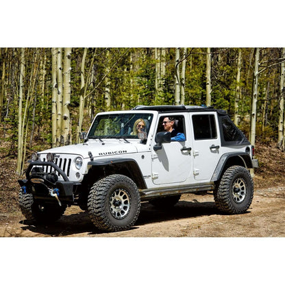 Jeep Rubicon with two people inside driving through a forest, showcasing adventure and outdoor experience.