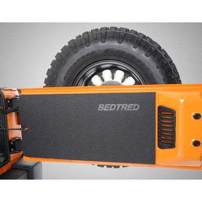 BedRug 2018-2026 Jeep Wrangler Tailgate Mat - Charcoal (BTJLTG) installed on Jeep with rugged tire background.